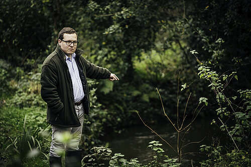 Jack Davies faces the camera whilst pointing to a river behind him